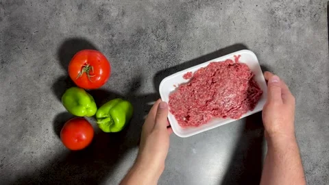 Man puts minced meat in white PVC packaging. Vegetables on kitchen table Stock Footage 297207889