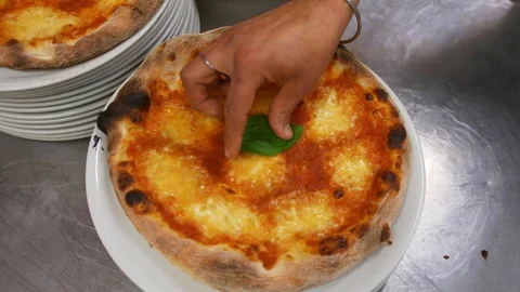 Man puts a mint leaf in middle of the pizza, which lies on pile of white plates. Stock Footage 104668477