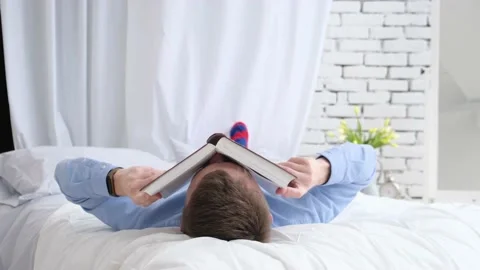 A man puts an open book on his head while lying on a bed Video stock 169227945