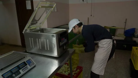 A man puts a packet of potatoes in a vacuum packer. Stock Footage 89615151
