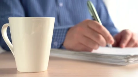 Man Puts A Pen On A Stack Of Papers And Takes A Mug Of Drink. Stock Footage 167885596