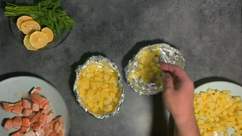 Man puts pieces of chopped potatoes into foil plate for baking in oven Stock Footage 293626060