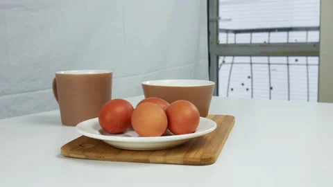 A man puts a plate with eggs on the table. White table, mug, bowl Stock Footage 102129834