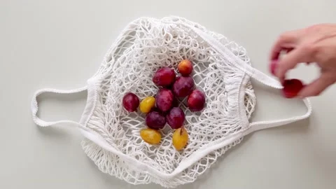 A man puts Plums in string eco mesh bag. Close up of man hands puts Plums Video stock 219917701