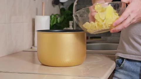 The man puts potatoes cut into thin slices into bowl of slow cooker. Fast Stock Footage 224516201