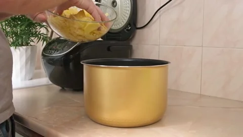 The man puts potatoes cut into thin slices into bowl of slow cooker. Fast Stock Footage 231517730