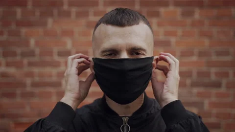 Man puts on protective covid mask, against brick wall, turns away from camera Stock Footage 163954663