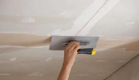 A man puts putty on a plasterboard ceiling. Putty for the joints of plaster.. Foto stock