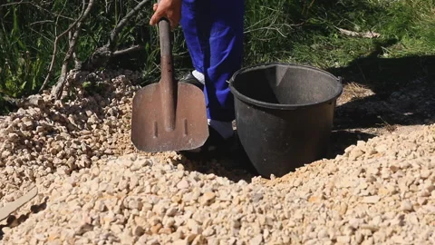 A man puts rubble from a pile into a bucket with a shovel Stock Footage 277395132