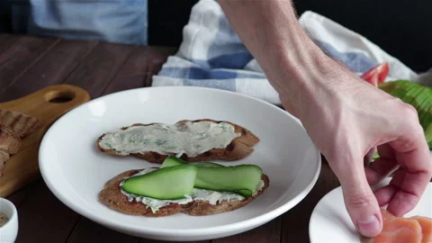Man puts salmon slice on   healthy sandwich with cucumber Stock Footage 130366298