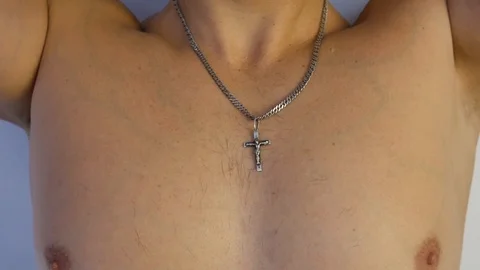 Man puts on a silver chain with a cross on his neck. Church symbol close up Stock Footage 122804717