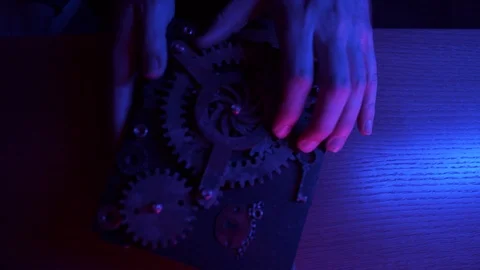 A man puts a small black box with gears on cover on a large wooden table. Puzzle Stock Footage 111699814