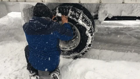 A man puts on snow chains that help tires get good traction in the snow and ice. Stock Footage