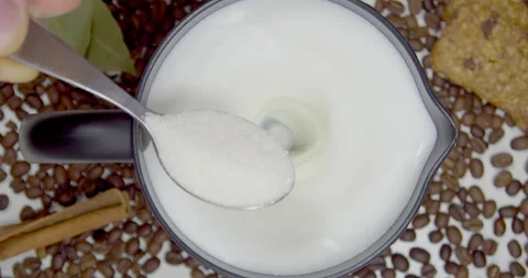 A man puts a spoonful of sugar in a rotating hot milk foam in a cappuccino maker Stock Footage 165670124