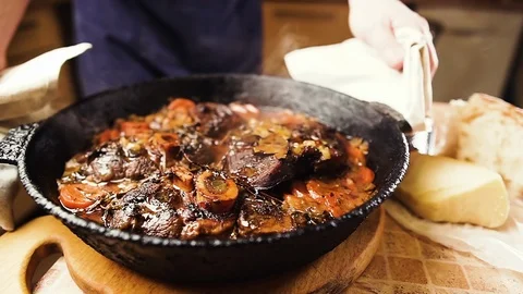 Мan puts on a table a pan with boiling ossobuco. Traditional italian food. Stock Footage 125706551