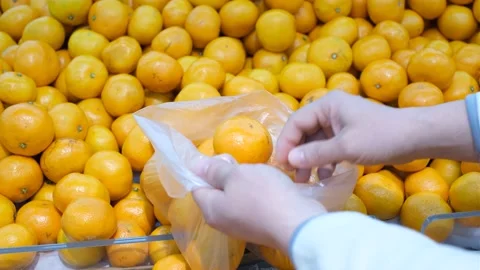 A man puts tangerines in a plastic bag in a supermarket, close-up. Stock Footage 166877847