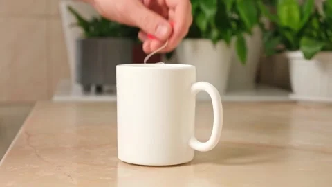 A man puts a tea bag in a white teacup to make himself some tea in kitchen Stock Footage 244677957