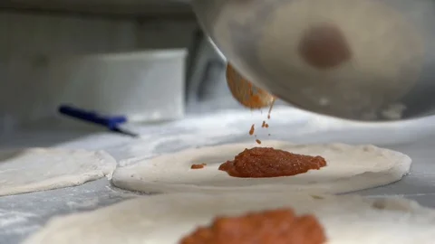 A man puts tomato paste in a circle of pizza dough. Flour scattered on the table 스톡 동영상 104865945