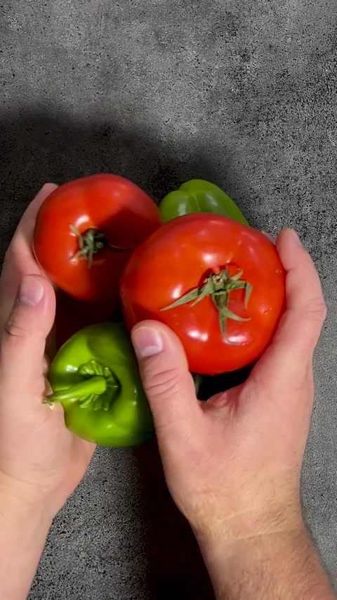 Man puts vegetables, red ripe tomato, green bell pepper on gray kitchen table Stock Footage 300651698