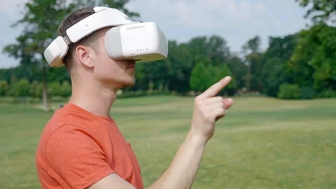 A man puts a VR headset on his head in a park and starts using Stock Footage 112805950