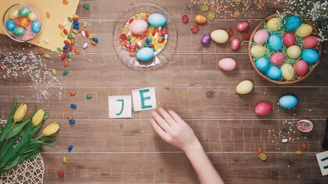 Man puts word Jesus on table decorated with easter eggs. Top view Stock Footage 73946752