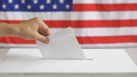 Man putting a ballot into a voting box. USA American flag on the background. Video stock 245445004