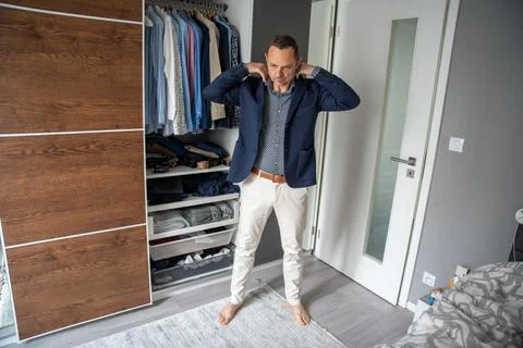 Man putting on a blue jacket in front of an open wardrobe. Getting dressed and Stock Photos