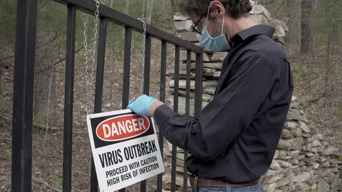 Man putting up a danger virus outbreak warning sign on a gate Video stock 128453934