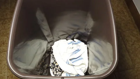 A man putting dirty laundry in a plastic bin Stock Footage 220746643