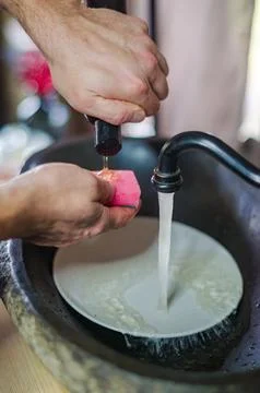 A man putting dish soap on a sponge to wash a white plate in the kitchen Stock Photos
