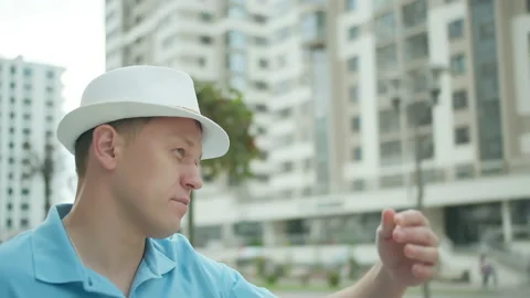Man putting on hat while standing on the street, buildings background Stock Footage 155456819