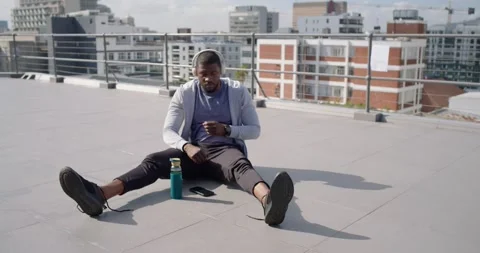 Man putting on headphones after checking phone and tying laces on rooftop Stock Footage 337943935