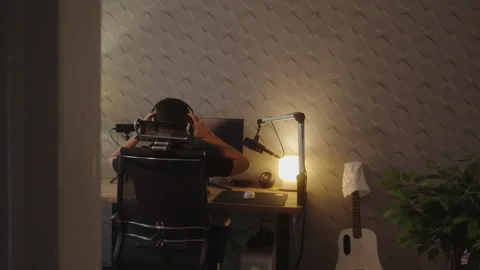 Man Putting On Headphones While Sitting at Computer Desk Stock Footage 327782896