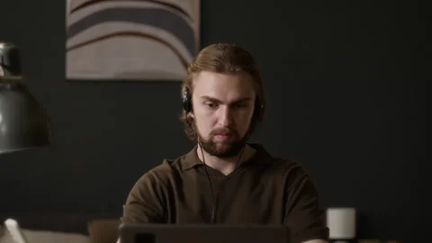 Man Putting on Headset for Remote Work on Laptop at Home Stock Footage 345516219