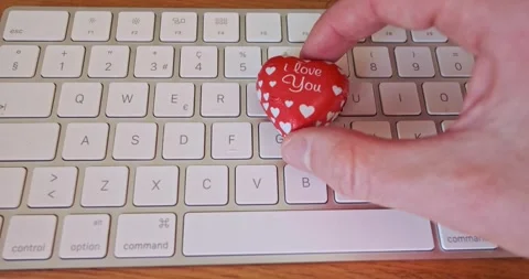 Man putting a heart-shaped chocolate candy on a computer keyboard Stock Footage 337998748
