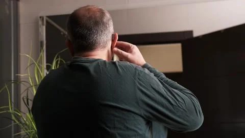 Man putting his hearing aids correctly in front of a mirror in the bathroom Stock Footage 266672749