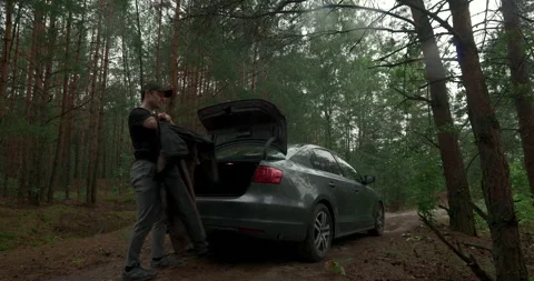 Man putting on jacket near open car trunk in rainy forest, audio included Stock Footage 340844368