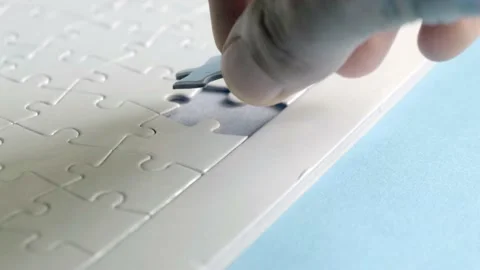 Man putting last piece of completely blank, white jigsaw puzzle Stock Footage 158944431