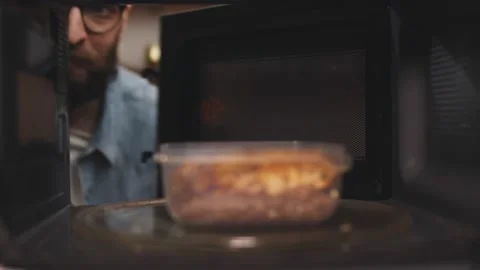 Man putting leftover dinner into microwave oven to cook Vidéo 145844413