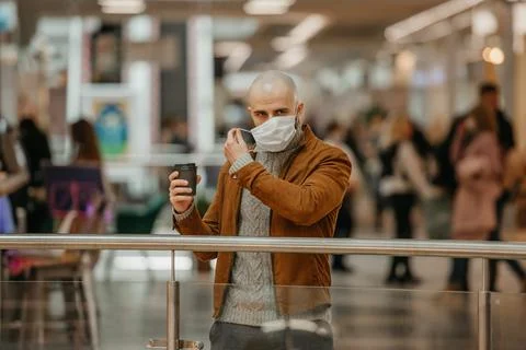 A man is putting on a mask while holding a cup of coffee in the shopping cent Stock Photos