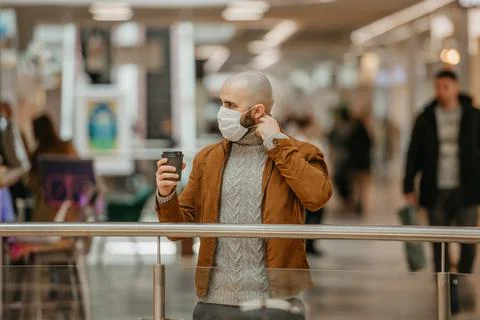 A man is putting on a mask while holding a cup of coffee in the shopping cent Stock Photos
