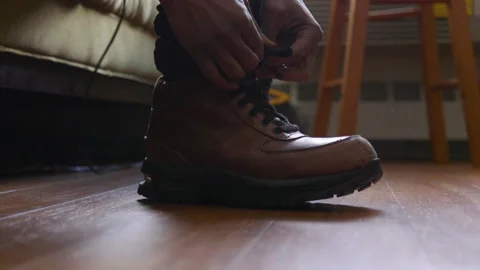 A man putting on a pair of leather boots, tying up the shoelaces, and then Stock Footage