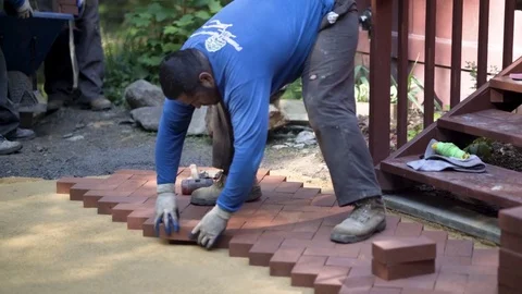 Man putting red brick pavers into place in a herringbone pattern on a bed of Stock Footage 81996809
