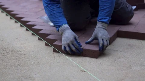 Man putting red brick pavers into place in a herringbone pattern on a bed of Stock Footage 82001883