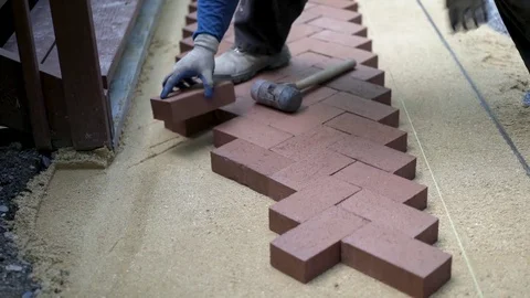 Man putting red brick pavers into place in a herringbone pattern on a bed of Stock Footage 82012072