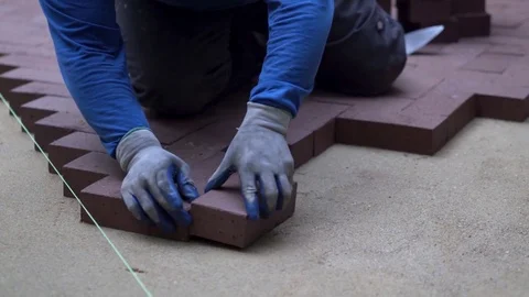 Man putting red brick pavers into place in a herringbone pattern on a bed of Stock Footage 82012132