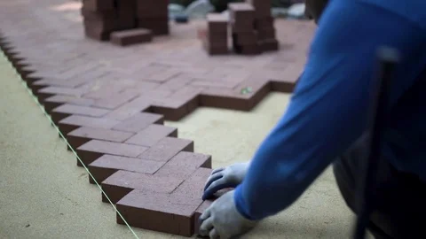 Man putting red brick pavers into place in a herringbone pattern on a bed of Stock Footage 82017379
