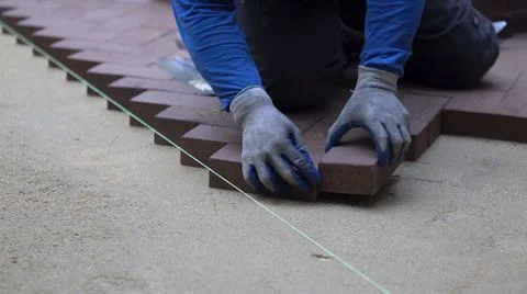 Man putting red brick pavers into place in a herringbone pattern on a bed of Stock Photos