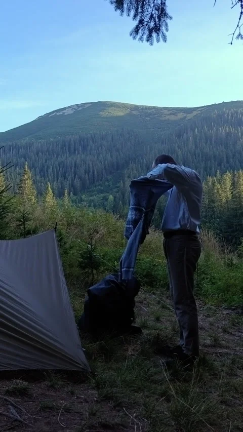 Man putting on warm wool sweater near camping tent in mountains 스톡 동영상 344877284