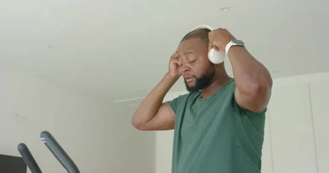 Man putting on white headphones, adjusting them, mounting exercise bike at home Stock Footage 342392833